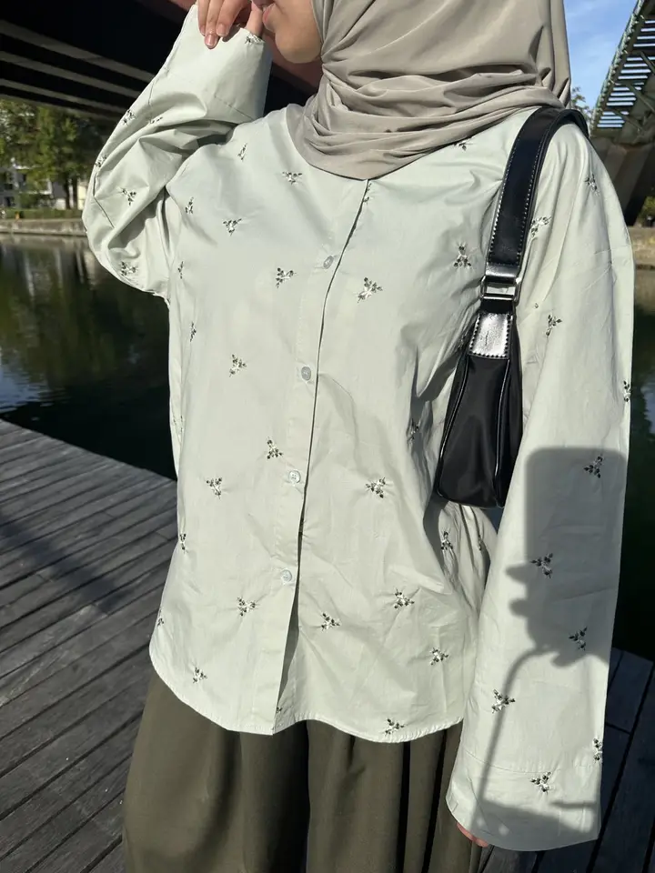 Chemise brodée vert sauge, portée avec un sac noir